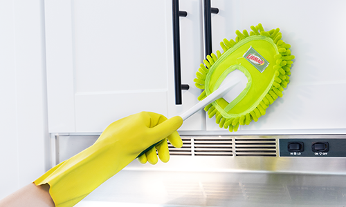 Person wearing yellow rubber glove cleaning cabinet doors with duster tool