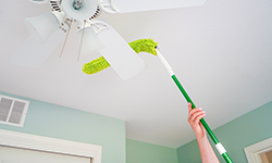 Person using long dusting wand to clean ceiling fan blades