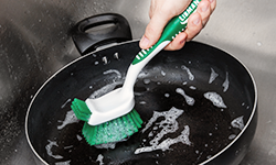 Person using dish brush to clean pan in sink