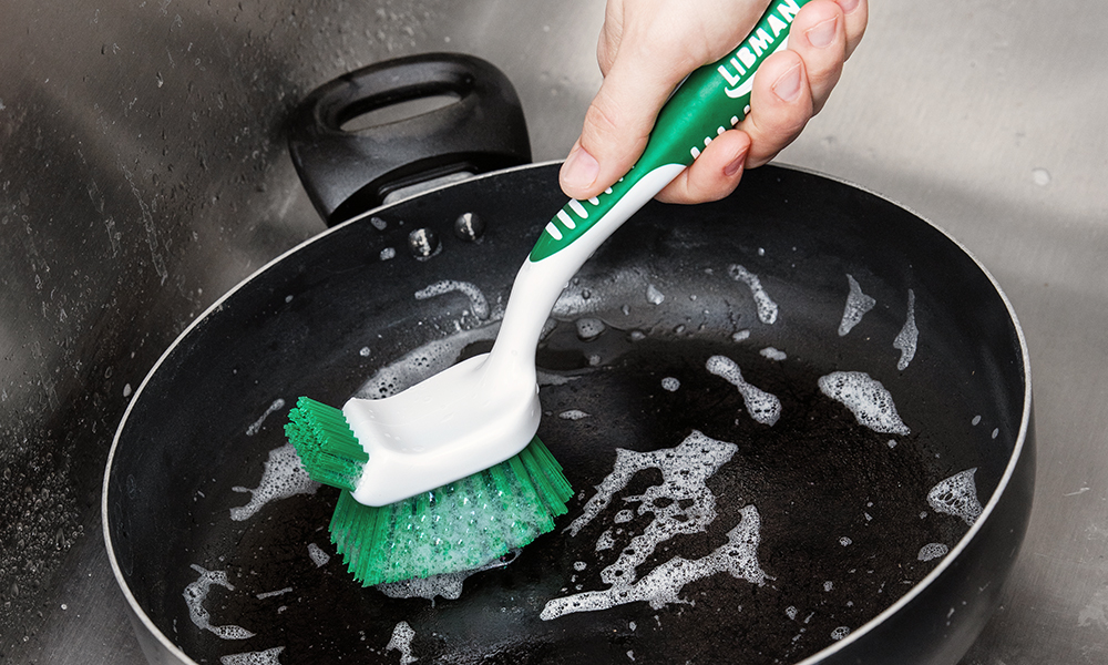 Person cleaning pan with dish brush