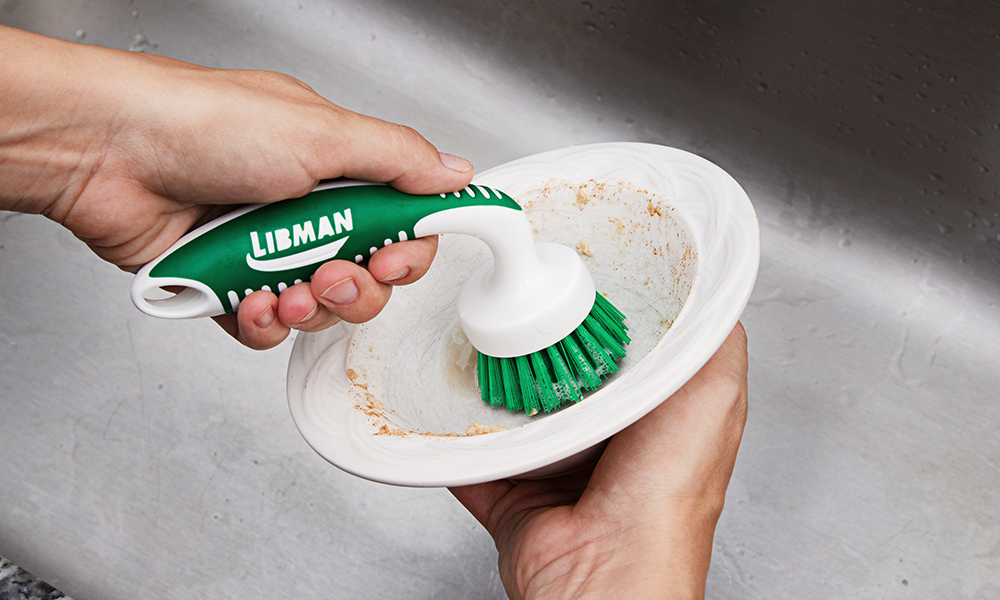 Person cleaning bowl with dish brush