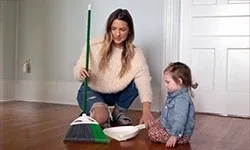 Mother and daughter using broom and dustpan to clean up