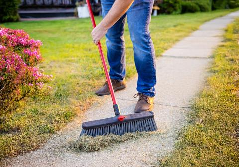 Person sweeping up grass on a sidewalk