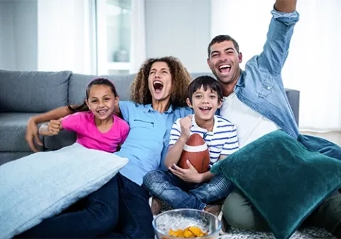 A family of four sitting on a sofa, cheering on a football team from home.